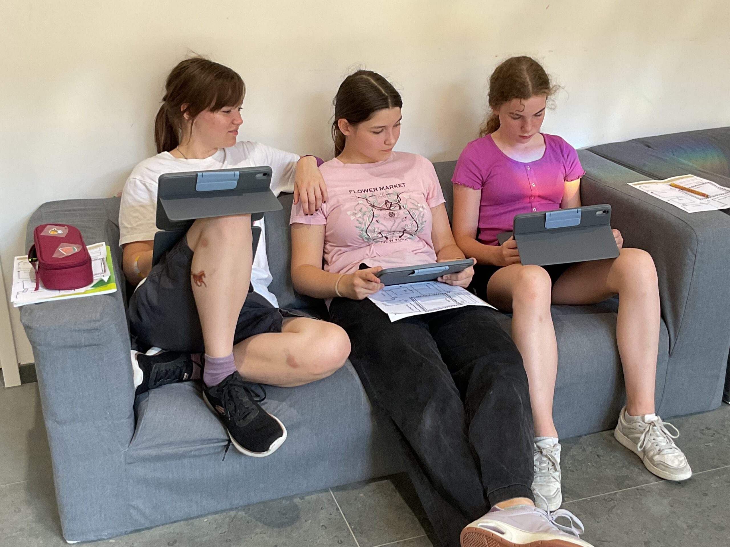 Drei Schülerinnen sitzen mitbIhren Tablets auf einer Couch.
