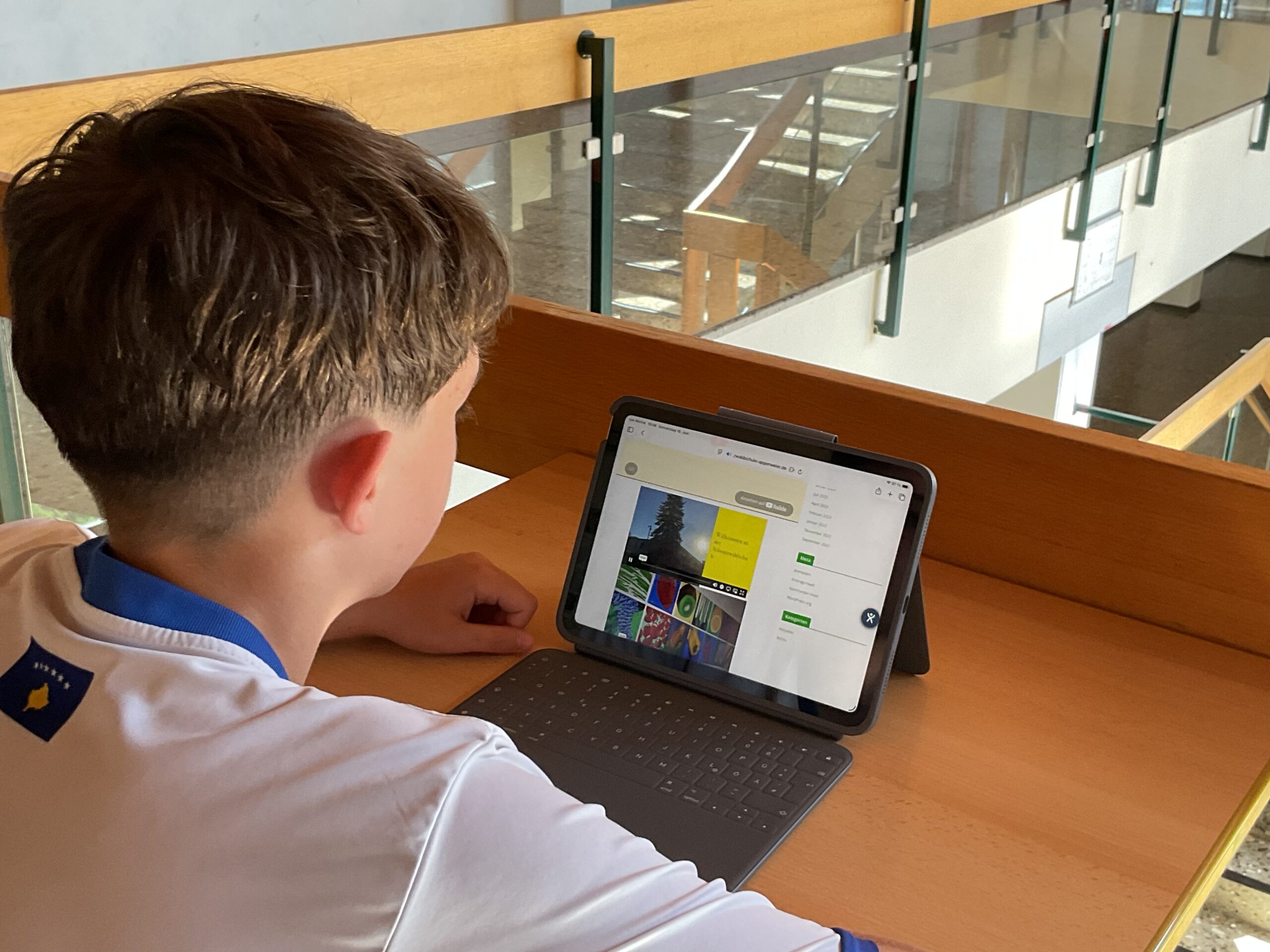 Ein Schüler sitz im Schulflur an einem Schreibtisch und lernt am Tablet.