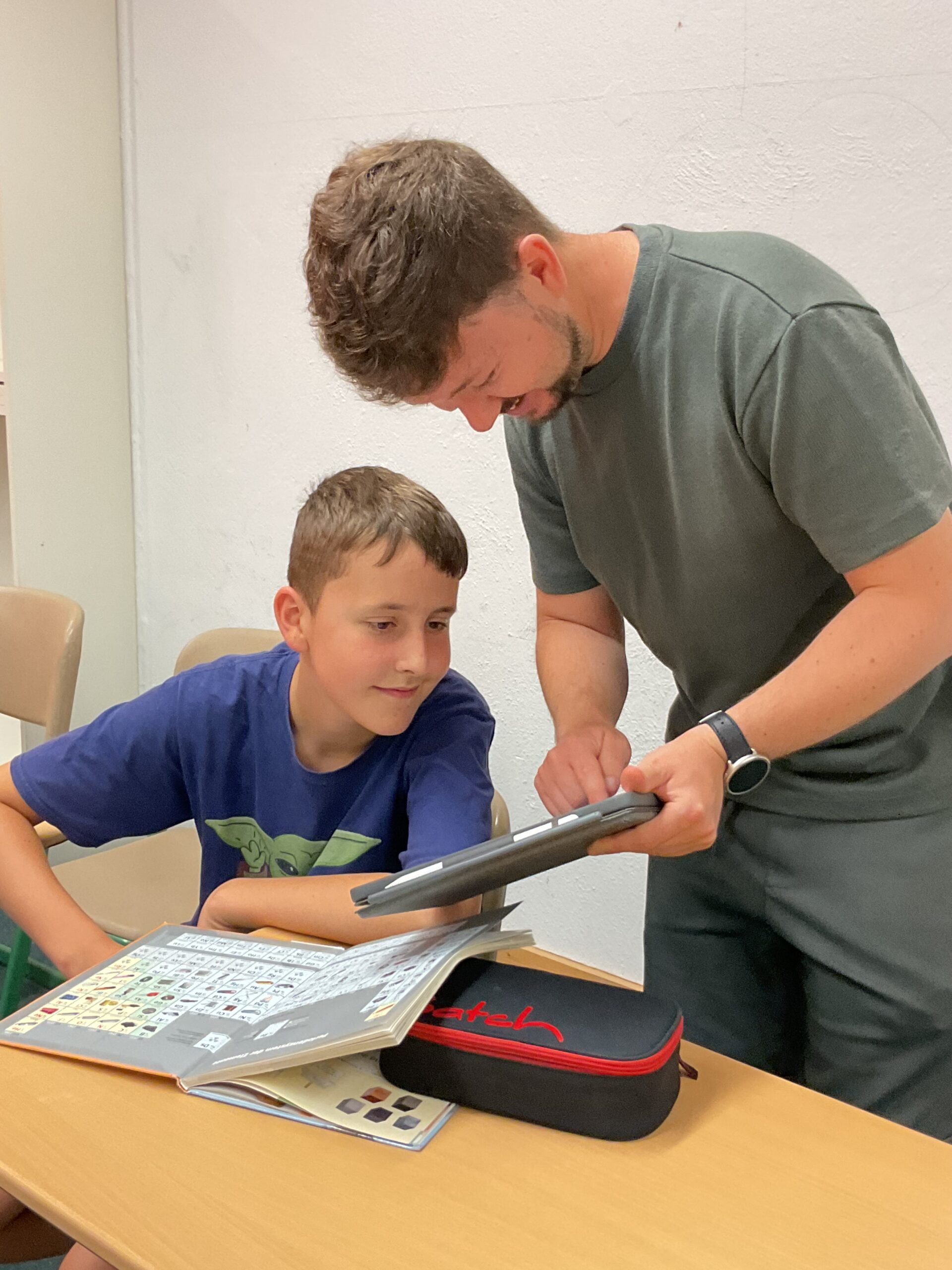 Lehrer zeigt einem Schüler etwas auf einem Tablet.