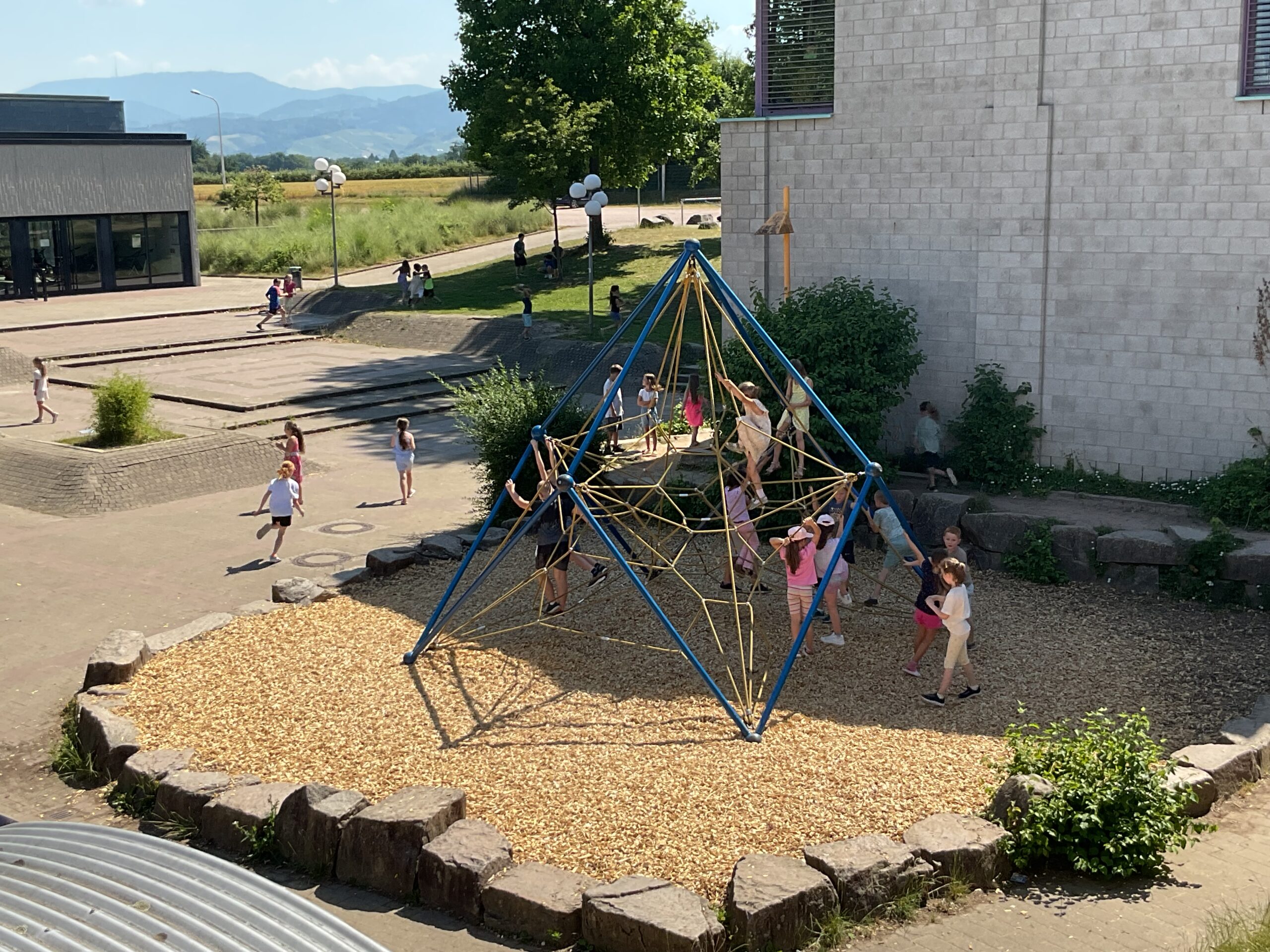 Kinder spielen im Schulhof, es gibt ein Klettergerüst.