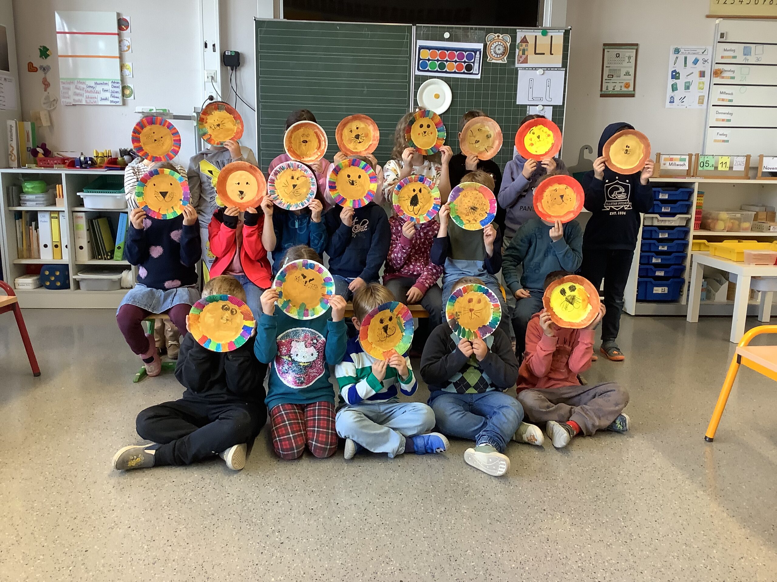 Eine Schulklasse hat auf Papptellern Löwengesichter gemalt die Kinder haben Sie zum Gruppenfoto vors Gesicht.