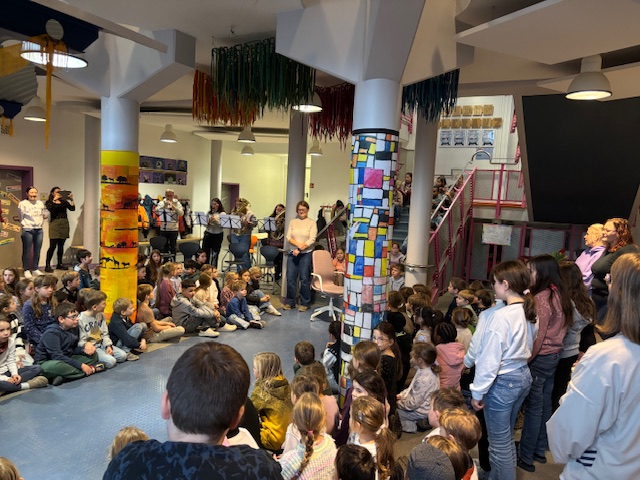 in der Eingangshalle sitzen alle Schüler au dem Boden, im Hintergrund wir mit Blasinstrumenten Musik gemacht.