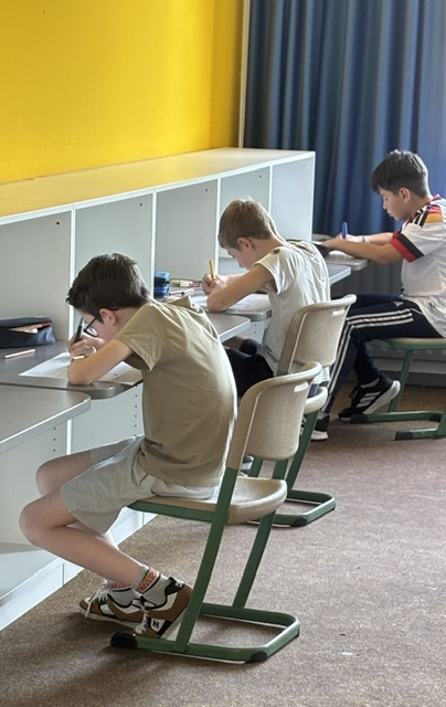 Kinder sitzen an Schreibtischen und schreiben.