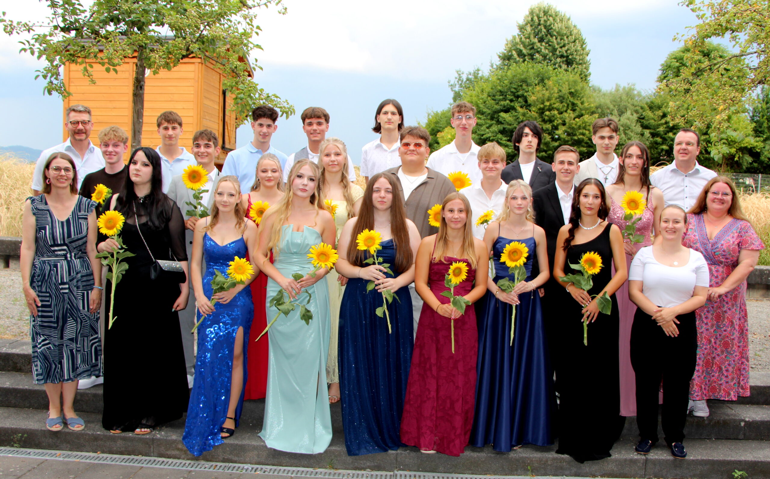 Abschlussklasse 10 mit Lehrer beim feierlichen Abschlussbild. Jeder Schüler hält eine Sonnenblume.