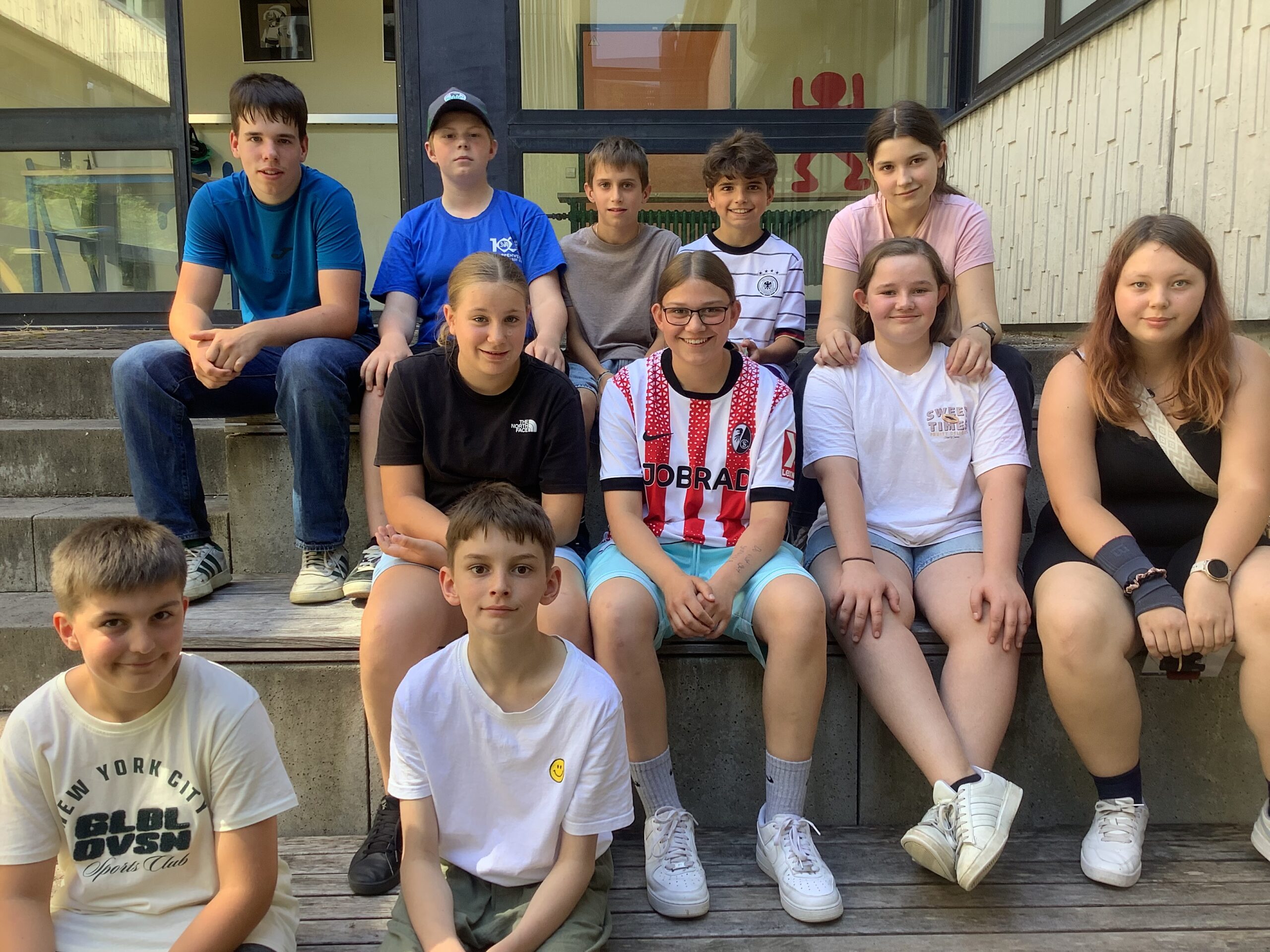 11 Schüler sitzen auf einer Treppe und schauen in die Kamera.
