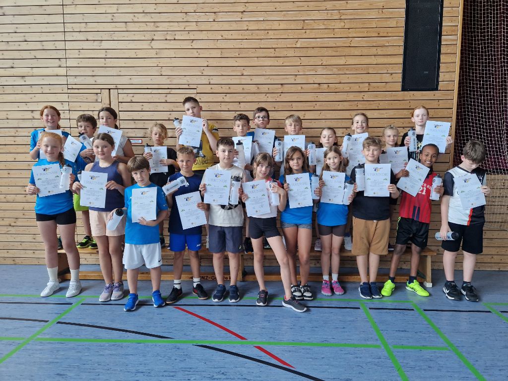 23 Schüler mit Urkunden stehen in der Sporthalle und lachen in die Kamera.